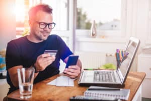 Young man at home office using credit card on his mobile phone